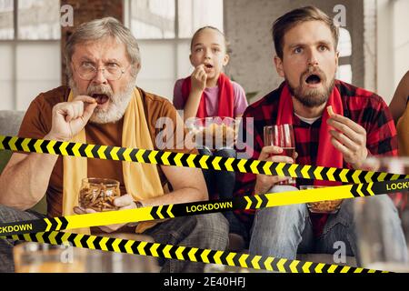 Cancellation. Soccer, football fans with snacks cheering for favourite sport team at home, behind the limiting tapes with Lockdown. Look disappointed, sad, angry. Blocked social life, group meetings. Stock Photo
