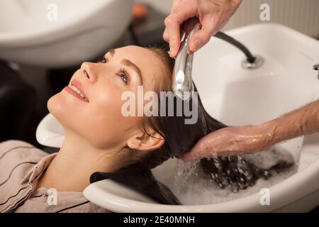 Close up cropped shot of a beautiful happy woman smiling, professional hairstylist washing her hair. Charming woman getting her hair prepared for new Stock Photo