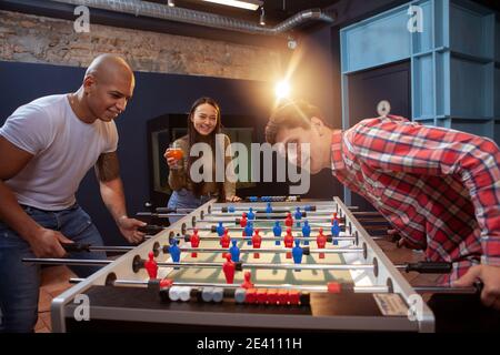 Group of young cheerful people enjoying playing table footbal at the cafe. Competition, friendship concept Stock Photo