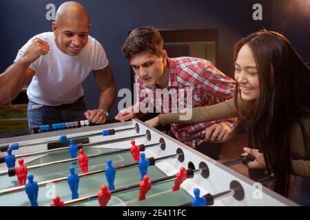 Multiethnic group of young friend having fun at beer pub, playing table soccer Stock Photo