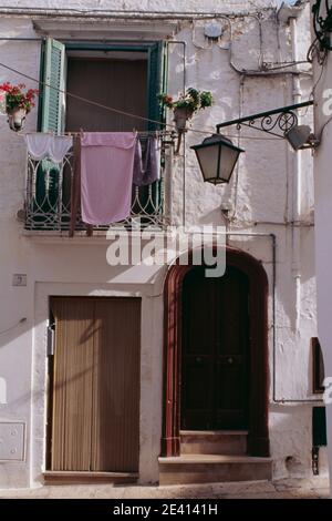 In old town, whitewashed houses, balcony with washing hung over, turquoise shutters, plants, street lamp on corner bracket, bead curtain over doorway Stock Photo