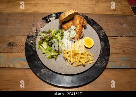 A delicious plate of Smoked Haddock Fish Finger sandwich with Fries and Tartar Sauce on a wooden kitchen table Stock Photo