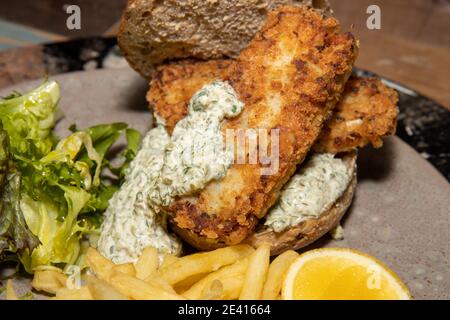 A delicious plate of Smoked Haddock Fish Finger sandwich with Fries and Tartar Sauce on a wooden kitchen table Stock Photo
