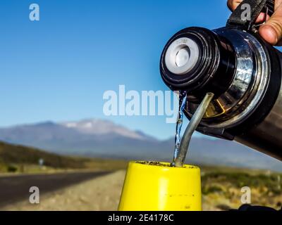 A person pouring water from a thermos into a yellow cup with mountains in the background Stock Photo