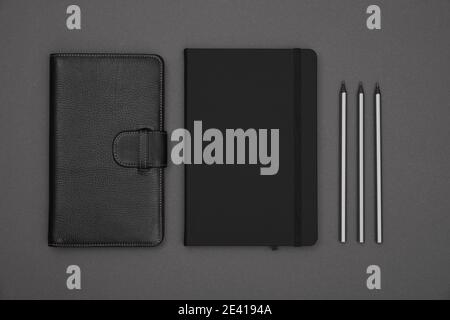 Close up two closed black leather cover notebooks and pencils over grey paper background, flat lay, directly above Stock Photo