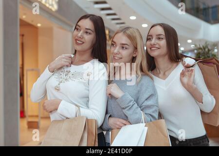 Group of beautiful cheerful female friends smiling, looking at the display of a store at local shopping mall. Lovely women carrying shopping bags, wal Stock Photo