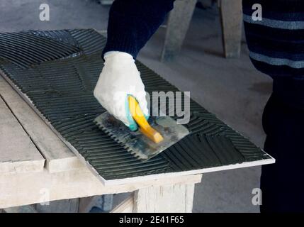 Close up of a builder, a tiler sitting in a glue spreading on a tile. Stock Photo