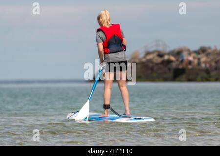 Bonnerup, Denmark - 15 Juli 2020: Girl on a surfboard, She has a paddle in her hand, and is equipped with safety equipment, The sun is shining and the