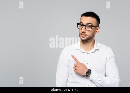 surprised hispanic businessman pointing aside with finger while looking at camera isolated on grey Stock Photo