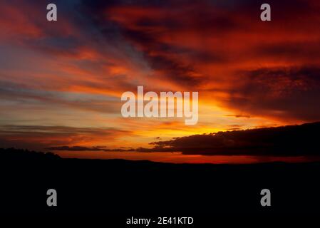 Fiery sunset. Evening sun on the horizon. The clouds are backlit with the bright red light. Pre-sunset twilight. Stock Photo