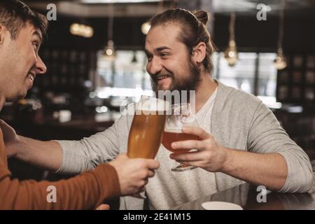 Cheerful bearded man telling jokes to his friend over a glass of beer at local irish pub. Happy man enjoying drinking beer with his brother. Two male Stock Photo