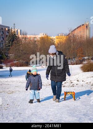 POZNAN, POLAND - Jan 17, 2021: Woman and child walking with wooden sled on white snow at a park on a cold winter day Stock Photo