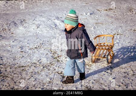 POZNAN, POLAND - Jan 17, 2021: Young boy pulling a wooden sled on snow at a park on a cold winter day. Stock Photo