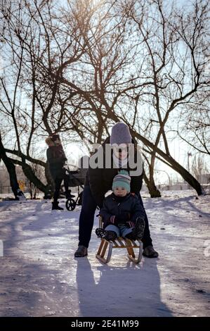 POZNAN, POLAND - Jan 17, 2021: Woman helping young boy on a sled at a park on a cold winter day Stock Photo