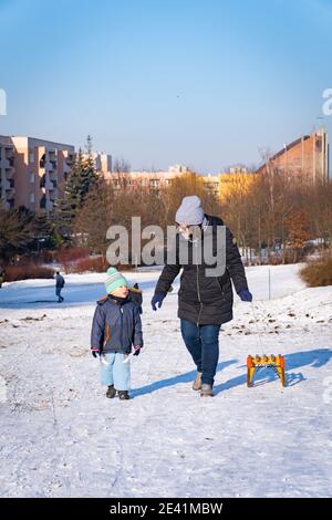 POZNAN, POLAND - Jan 17, 2021: Woman and child walking with wooden sled on white snow at a park on a cold winter day Stock Photo