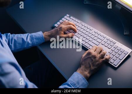 Close-up back view of man watching on monitor and working typing on wireless computer keyboard. Stock Photo