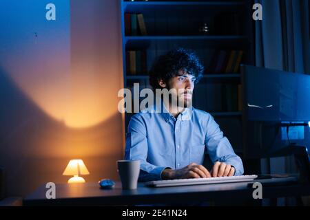 Portrait of smiling man looking intently at monitor screen while working on computer at late night. Stock Photo