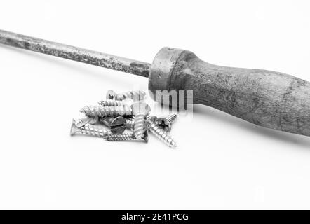 Grayscale shot of metal screws and screwdriver isolated on white background Stock Photo