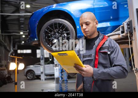 Handsome African man writing on his clipboard, working at the garage, repairing cars Stock Photo