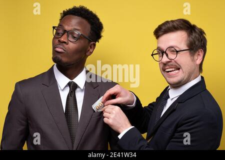 Caucasian man gives bribe in Euro banknotes. Corruption in business. Studio shot on yellow wall. Stock Photo
