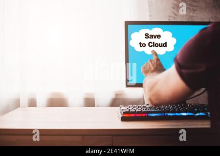A man creates a backup copy of data in the cloud storage - the inscription save to cloud on a computer monitor Stock Photo
