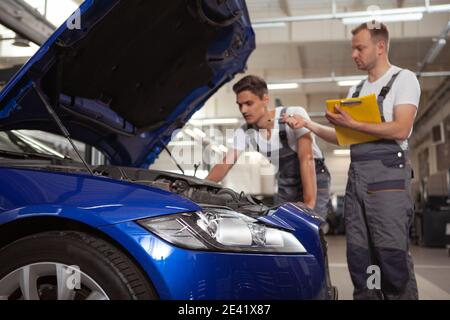 Selective focus on car lights, two mechanics examining engine of a car on background. Broken automobile at car service station Stock Photo