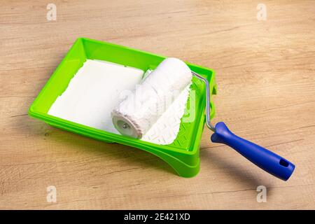 Paint roller in a green tray with white paint on a wooden background. Stock Photo