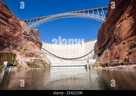 The Glen Canyon Dam holding back Lake Powell and the Glen Canyon Bridge with a clear blue sky background as seen from the surface of the Colorado Rive Stock Photo