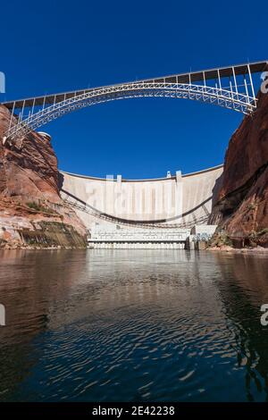 The Glen Canyon Dam holding back Lake Powell and the Glen Canyon Bridge with a clear blue sky background as seen from the surface of the Colorado Rive Stock Photo