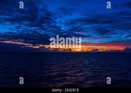 Dark clouds hang over the Pacific Ocean off Papua New Guinea, a narrow orange band marking the sunset on the horizon. Stock Photo