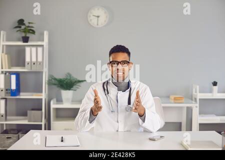 Young black man doctor therapist looking at camera and communicating with patient online Stock Photo