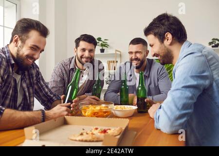 Group of friends eating pizza, drinking beer, telling jokes and having good time Stock Photo