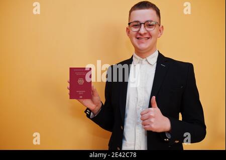 Young handsome man holding Federal Republic of Germany passport id over yellow background, happy and show thumb up. Travel to Europe country concept. Stock Photo