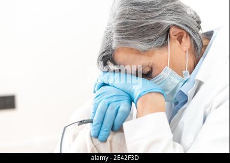 Tired senior female doctor resting head on her knees Stock Photo