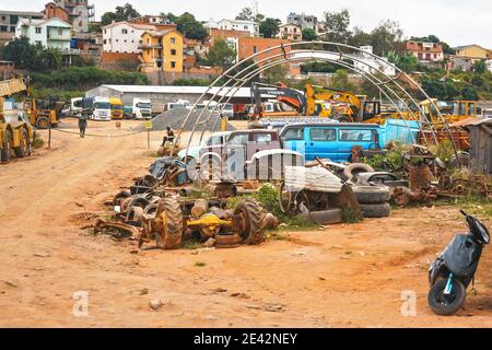 Antananarivo, Madagascar - April 24, 2019: Various automobile parts on red dust ground of small scrapyard near main road, trucks and construction vehi Stock Photo