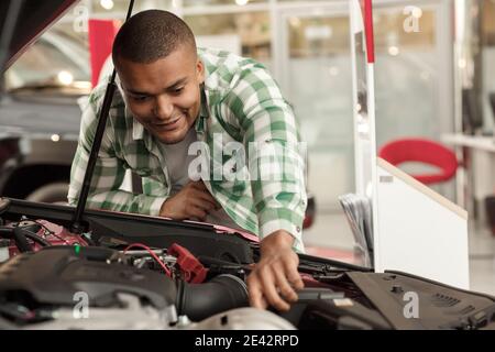 Male customer checking out engine of a new car for sale. Attractive cheerful man examining motor of an auto, while choosing vehicle to buy at the deal Stock Photo