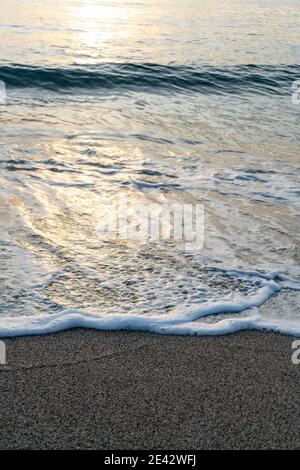 Waves breaking on a sandy beach, spray, white water and grass in foreground Stock Photo