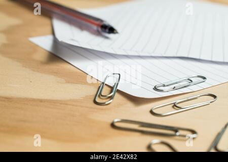 Metal paper clips and colorful  push pins with some sheets on a wooden table Stock Photo