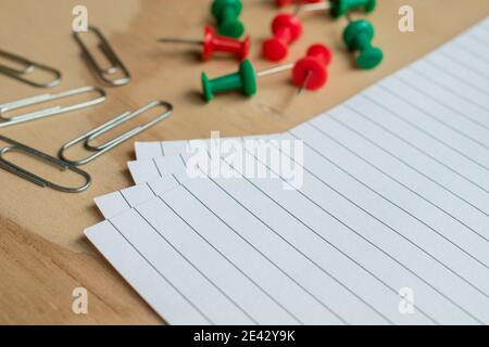Metal paper clips and colorful  push pins with some sheets on a wooden table Stock Photo