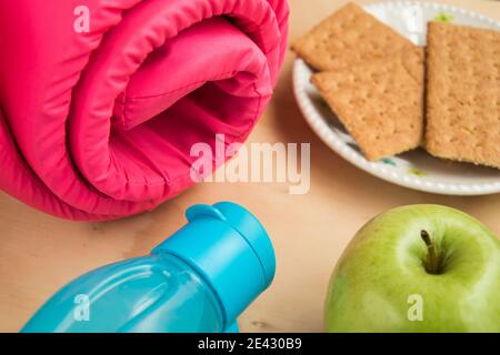 Pink yoga mat, green apple, some cookies and bottle on a wooden table Stock Photo