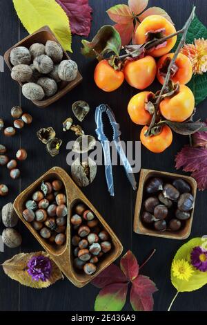 Hazelunts,walnuts ,chestnuts, persimmon fruits,a nutcracker, autumn leaves and flowers on wooden table Stock Photo