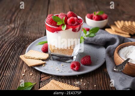 No bake cheesecake dessert in a glass jar topped with raspberry puree and fresh berries on rustic wooden background Stock Photo