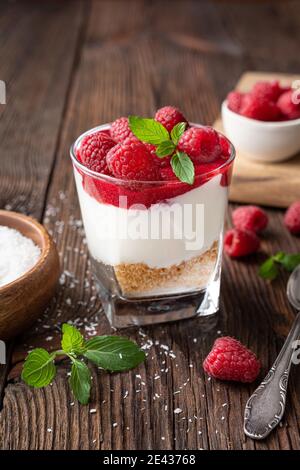 No bake cheesecake dessert in a glass jar topped with raspberry puree and fresh berries on rustic wooden background Stock Photo