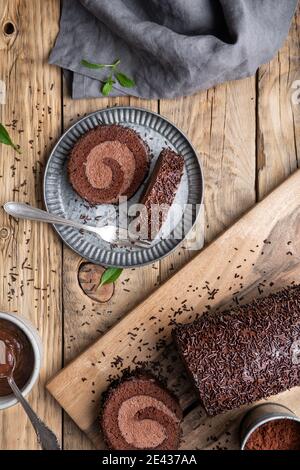 Chocolate cake roll with cocoa filling, topped with ganache glaze and sprinkles on wooden background Stock Photo