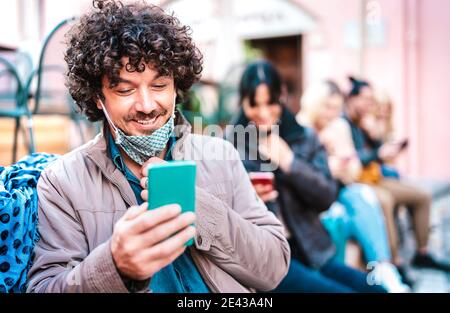 Happy millenial guy smiling over open face mask after lockdown reopening - Hipster man watching news on mobile smart phone Stock Photo