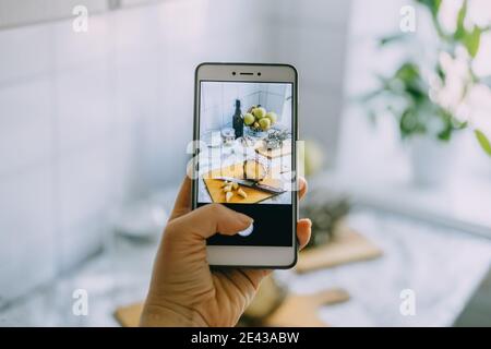 Food blogger takes photo on smartphone for social networks. Female hand holding cell phone with photo of cooking process of homemade Fermented Stock Photo