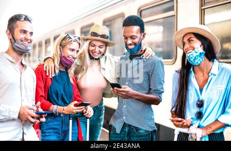 Friends group having fun with mobile smart phones while waiting for train at railway station - New normal travel concept about young people Stock Photo