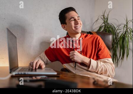 Young cheerful Hispanic male working on the computer and talking to someone Stock Photo