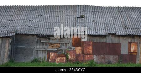 Old aged wooden shack grey plated wood boarding hut wall rusted metal rusty texture dark sky panorama grunge patches grungy gray roof damaged dirty Stock Photo