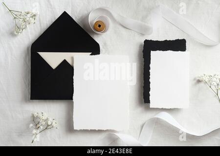 Wedding invitations mockups and black envelopes on textile background with flowers and white ribbon. Elegant wedding flat lay composition. Top view. Stock Photo
